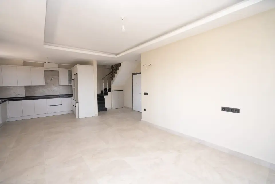 A living room with a kitchen and a staircase to the upper level of a penthouse